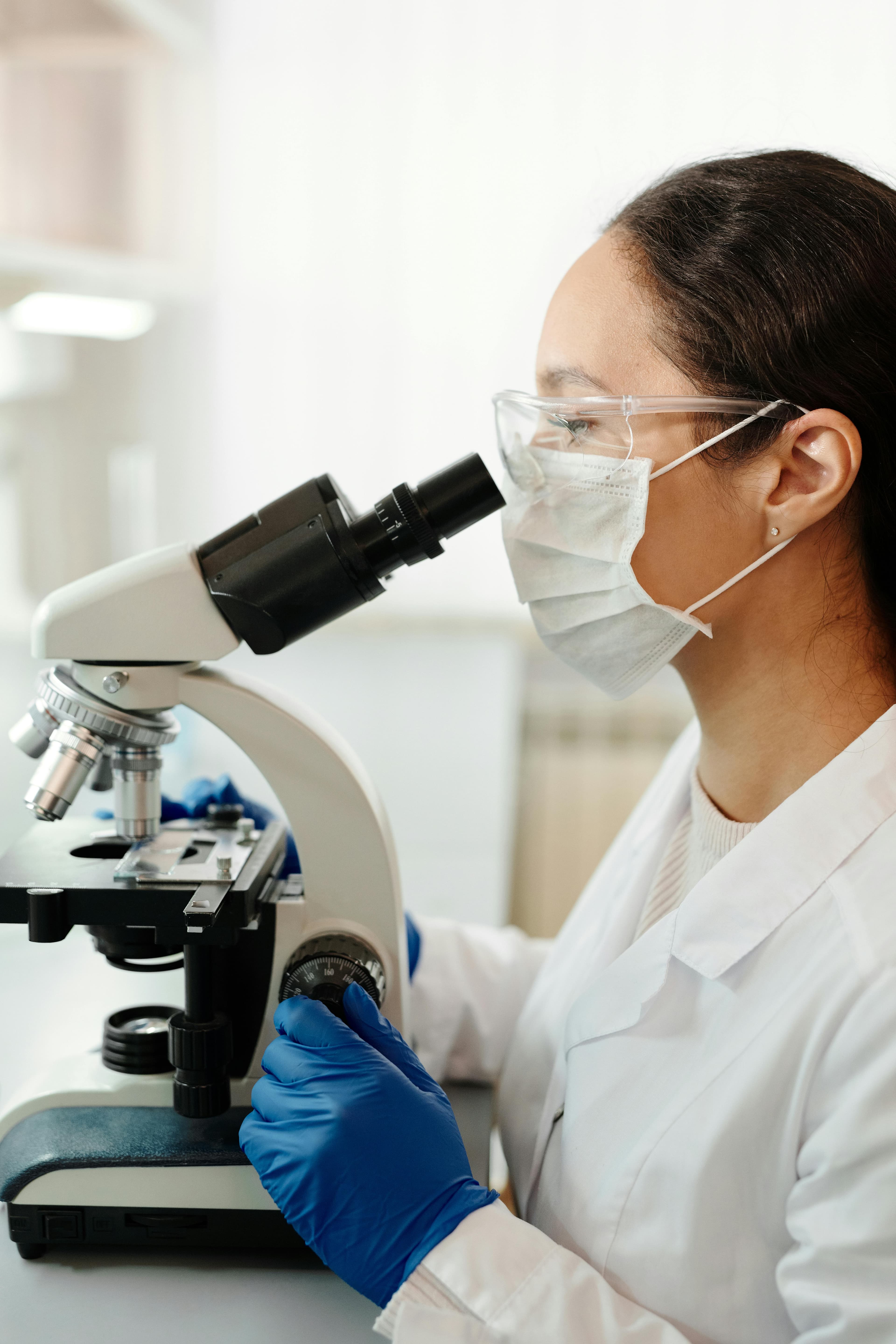 Laboratory researcher in safety glasses examining samples through a microscope.